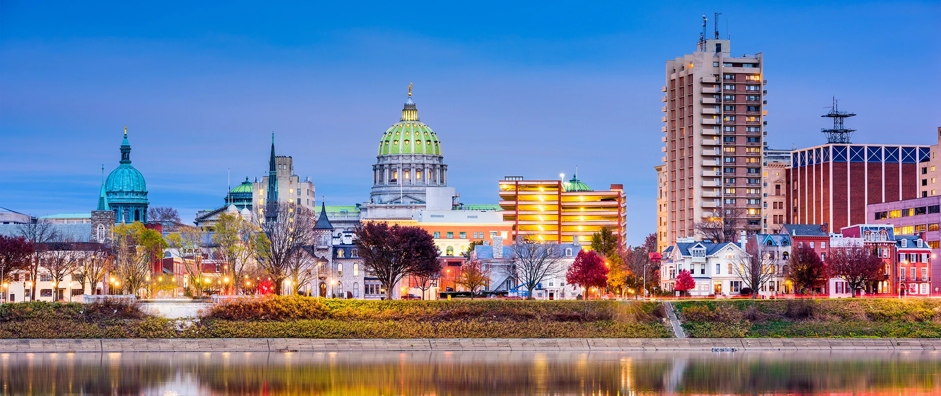 Twilight view of Harrisburg skyline featuring the State Capitol dome, historic buildings, and reflections on the Susquehanna River