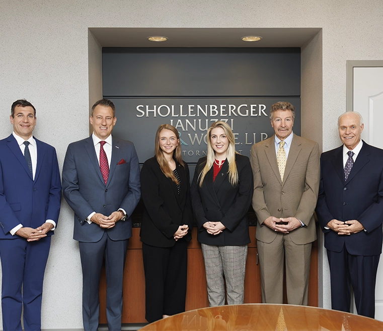A group of five professionals, dressed in formal attire, poses for a photo in an office setting with the company's name displayed behind them