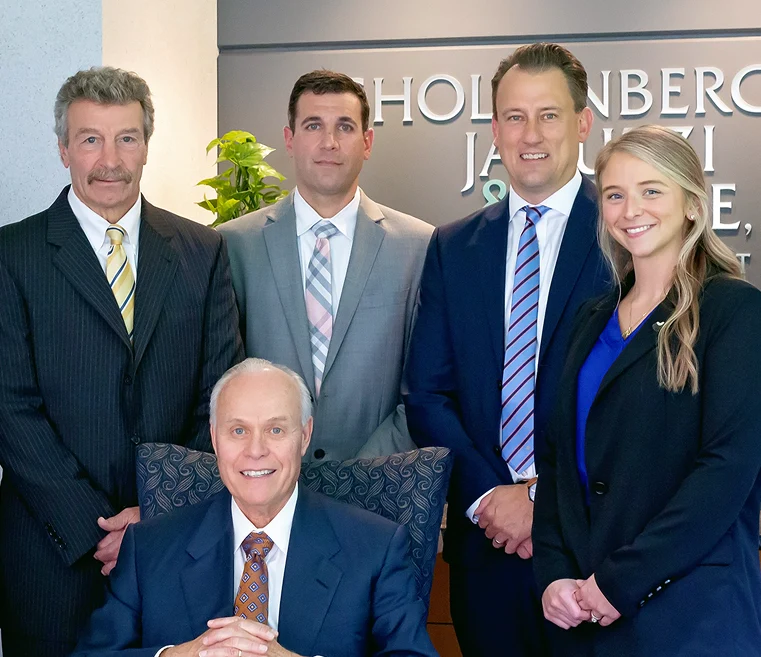 A group of five professionals, dressed in formal attire, poses for a photo in an office setting with the company's name displayed behind them